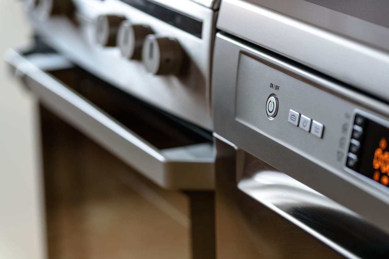 heros-img Close-up view of modern stainless steel kitchen appliances with focus on dishwasher and oven.
